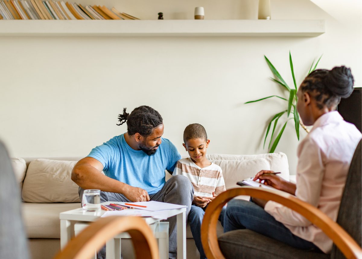 A father and son sitting with a counselor in a bright living room